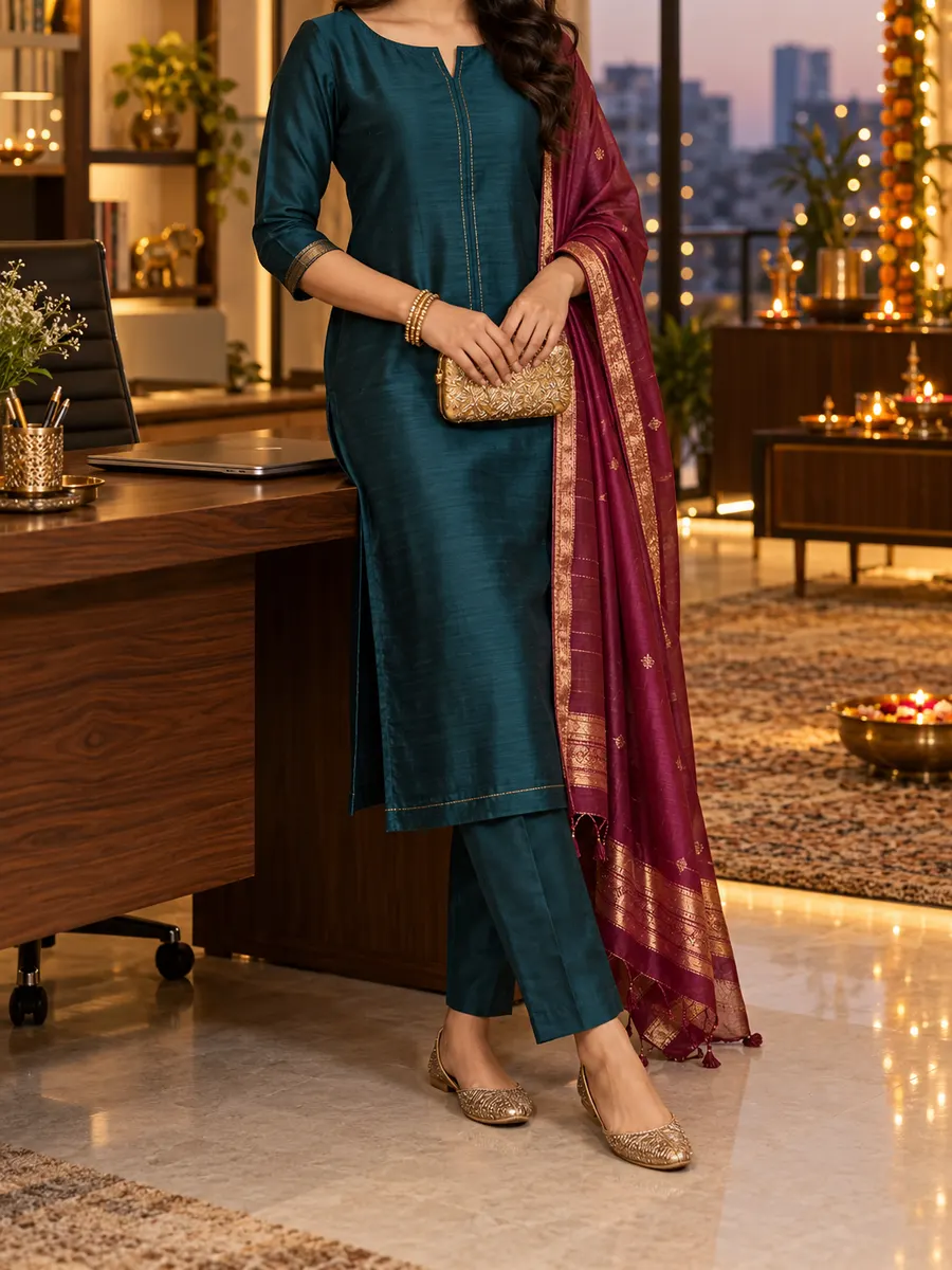 A woman in a teal kurta set with a berry Banarasi dupatta and a gold clutch, in an office lit with diyas for Diwali.