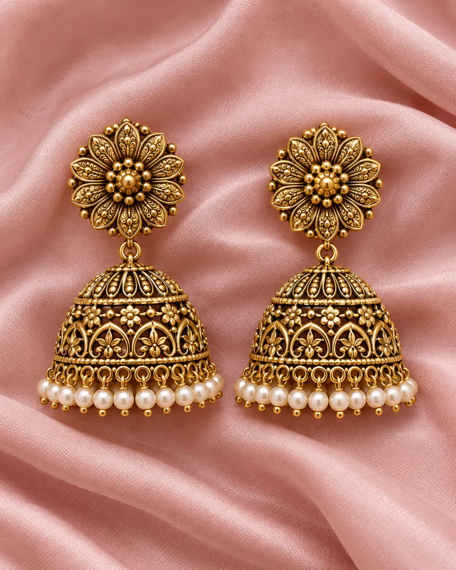 A pair of antique-gold temple jhumkas with flower studs, domed bells and pearl drops, on pink silk.